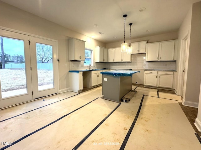 kitchen featuring white cabinetry, baseboards, hanging light fixtures, decorative backsplash, and a center island