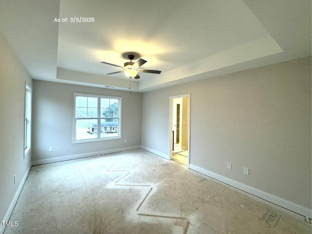 spare room featuring a ceiling fan, a tray ceiling, and baseboards