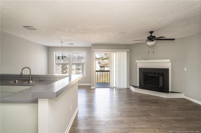 kitchen featuring a fireplace with raised hearth, ceiling fan, a sink, baseboards, and dark wood-style floors