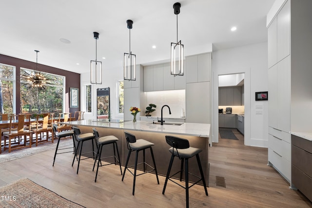 kitchen with gray cabinetry, sink, a notable chandelier, light hardwood / wood-style floors, and decorative light fixtures