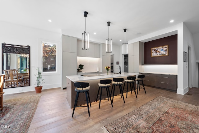 kitchen featuring gray cabinetry, sink, light hardwood / wood-style flooring, a large island, and a kitchen bar