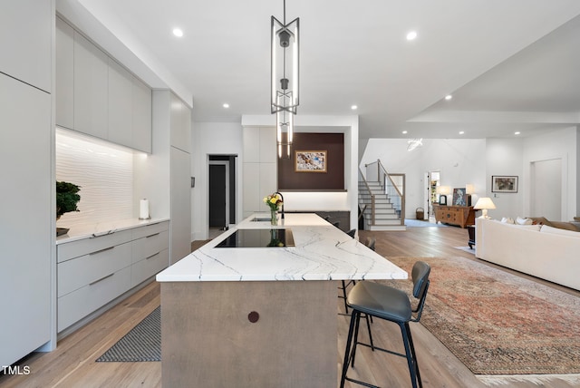 kitchen with pendant lighting, a spacious island, light wood-type flooring, and black electric cooktop