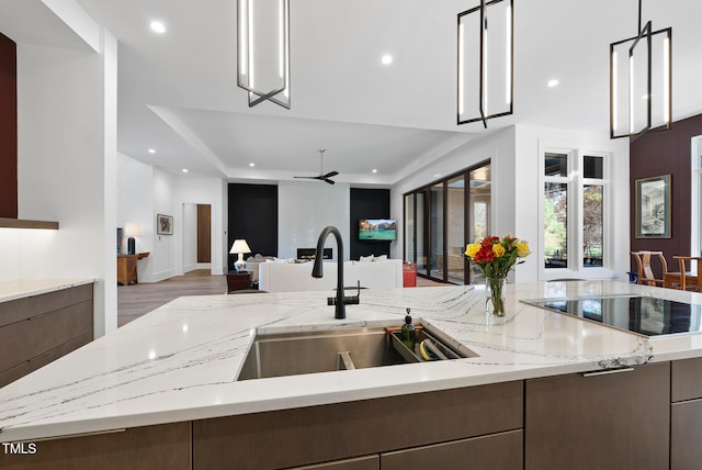 kitchen featuring light stone countertops, sink, light hardwood / wood-style floors, decorative light fixtures, and black electric cooktop