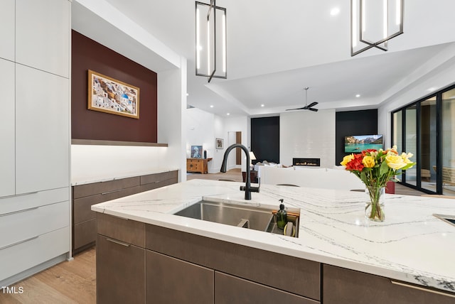 kitchen featuring white cabinetry, light stone countertops, sink, a fireplace, and light wood-type flooring