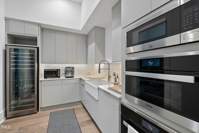 kitchen with sink, beverage cooler, decorative backsplash, appliances with stainless steel finishes, and light wood-type flooring