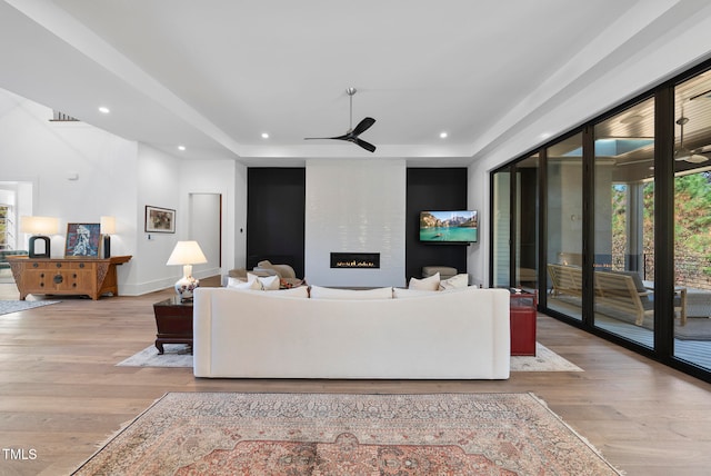 living room with a large fireplace, light hardwood / wood-style flooring, and ceiling fan