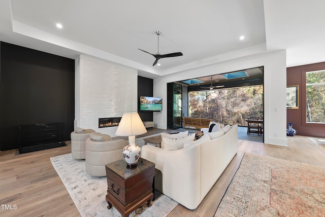 living room with ceiling fan, a large fireplace, and light wood-type flooring