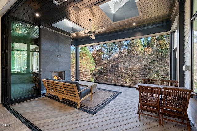 sunroom / solarium featuring a skylight, ceiling fan, a fireplace, and wood ceiling