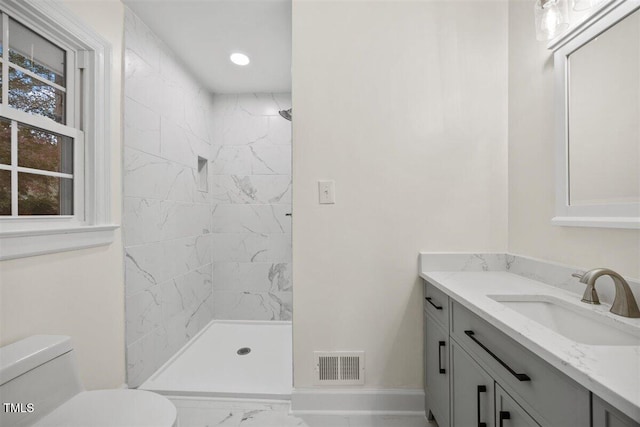 bathroom featuring a tile shower, vanity, and toilet