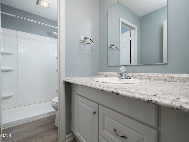 bathroom with walk in shower, vanity, a textured ceiling, hardwood / wood-style floors, and toilet