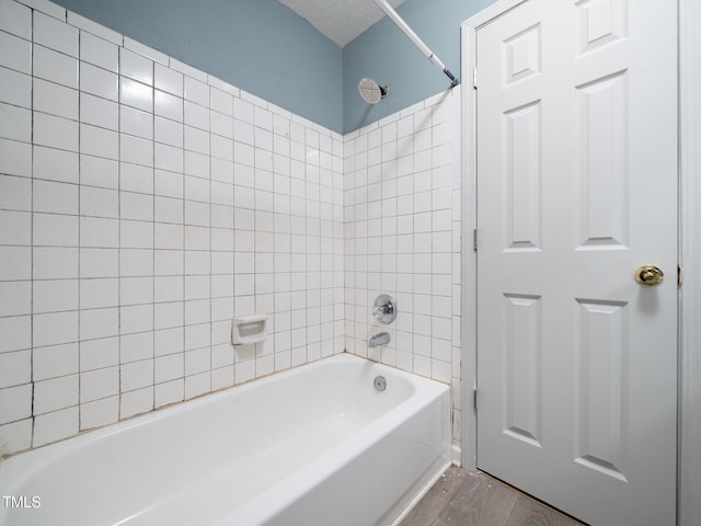 bathroom featuring a textured ceiling, wood-type flooring, and tiled shower / bath