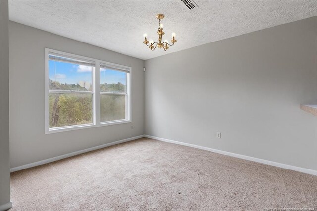 spare room with carpet flooring, a notable chandelier, and a textured ceiling