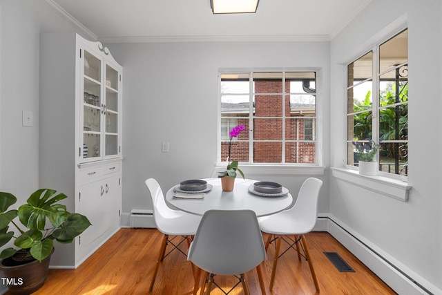 dining area with light wood-type flooring, crown molding, and a baseboard heating unit