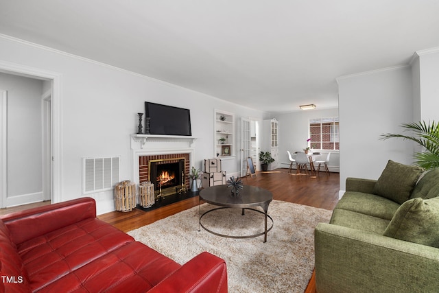 living room with built in shelves, crown molding, wood-type flooring, and a brick fireplace