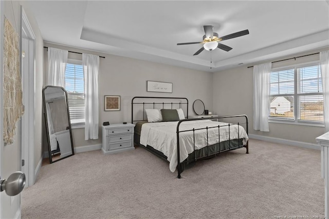 bedroom featuring light carpet, a tray ceiling, multiple windows, and ceiling fan