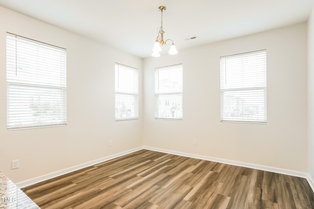 spare room featuring hardwood / wood-style flooring, plenty of natural light, and a chandelier