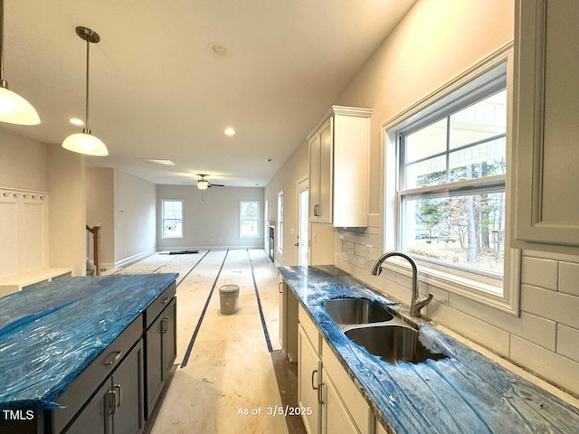 kitchen with pendant lighting, tasteful backsplash, open floor plan, a sink, and baseboards