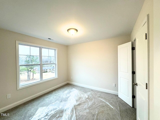 spare room with carpet floors, visible vents, and baseboards