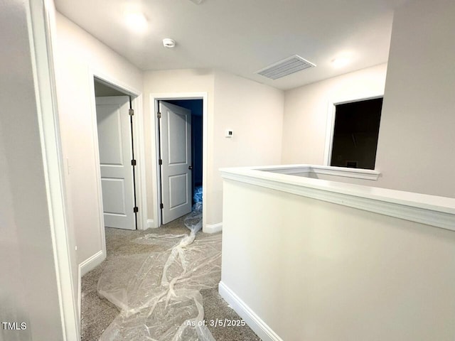 hall featuring light carpet, baseboards, and visible vents