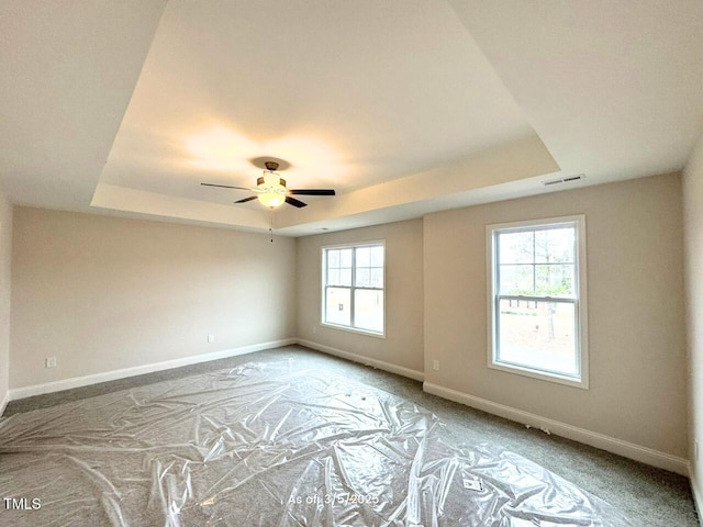 carpeted spare room with a ceiling fan, a raised ceiling, visible vents, and baseboards