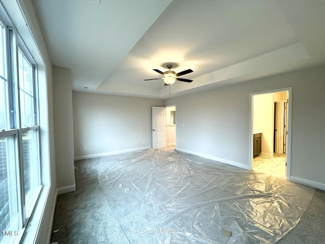 spare room featuring a tray ceiling, a ceiling fan, light colored carpet, and baseboards