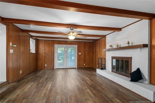 unfurnished living room with dark wood-type flooring, french doors, wood walls, beamed ceiling, and a fireplace