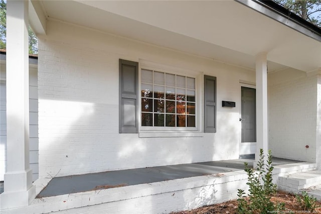 view of exterior entry with a porch and brick siding