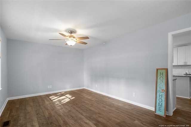 unfurnished room with baseboards, visible vents, dark wood finished floors, and a ceiling fan