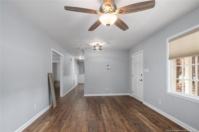 spare room featuring dark wood-style floors, a ceiling fan, attic access, and baseboards