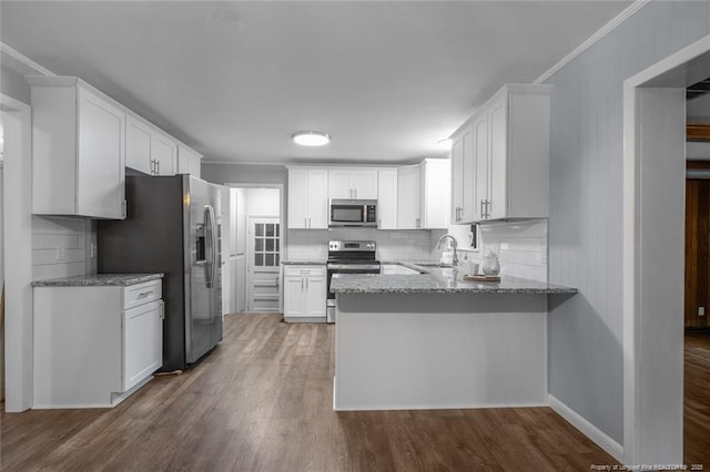 kitchen with light stone countertops, appliances with stainless steel finishes, white cabinetry, a sink, and wood finished floors