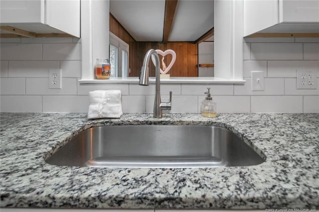 details featuring light stone countertops, decorative backsplash, white cabinets, and a sink