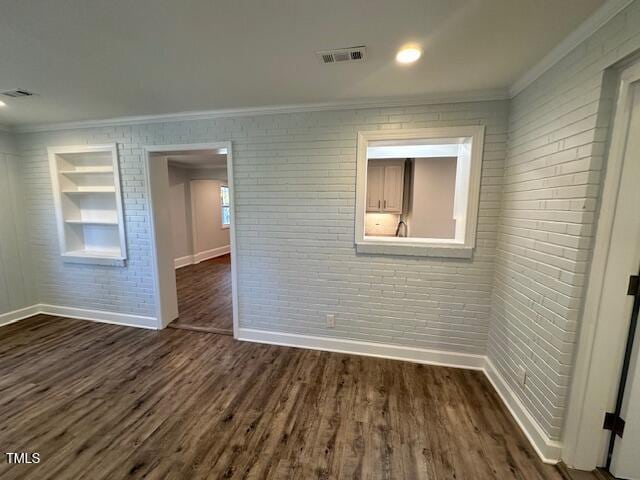 empty room with dark hardwood / wood-style flooring, crown molding, and brick wall