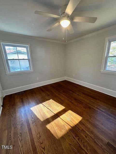 empty room with dark hardwood / wood-style floors, a wealth of natural light, and ornamental molding