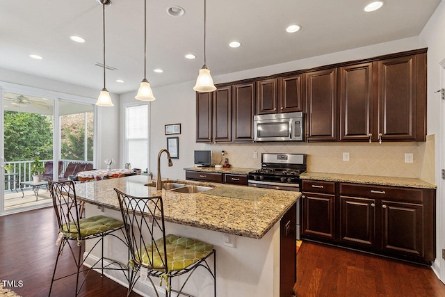 kitchen with an island with sink, stainless steel appliances, hanging light fixtures, and sink