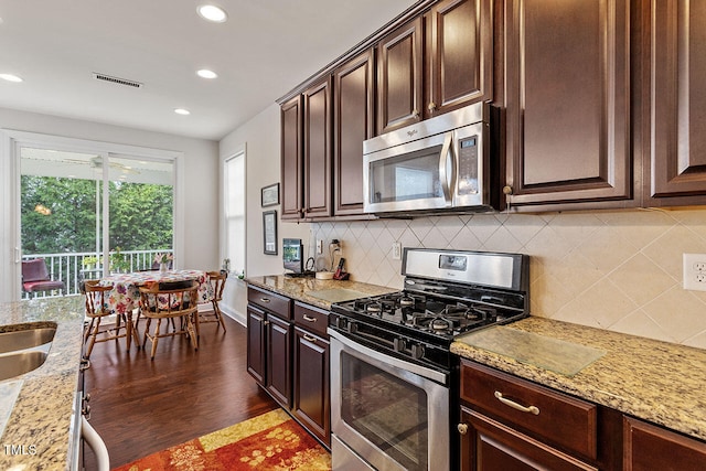 kitchen with backsplash, dark hardwood / wood-style floors, light stone counters, dark brown cabinetry, and stainless steel appliances