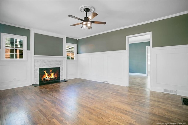 unfurnished living room with wood-type flooring, a stone fireplace, ceiling fan, and crown molding