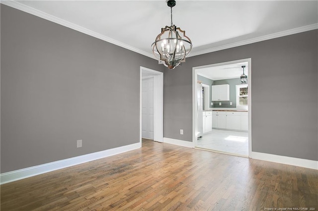 spare room featuring wood-type flooring, crown molding, and a notable chandelier