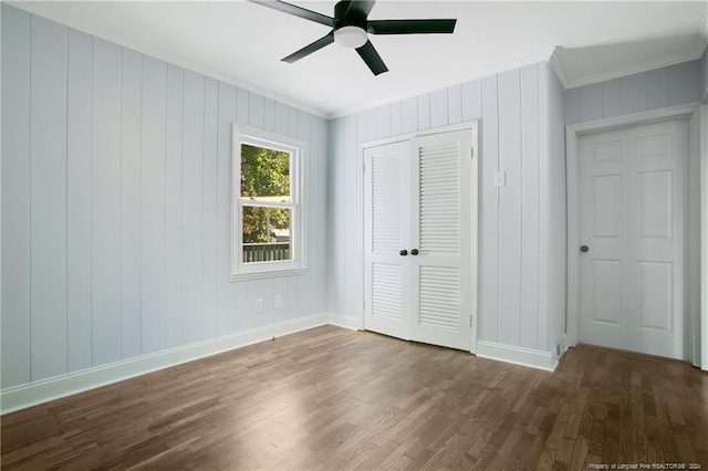 unfurnished bedroom with dark hardwood / wood-style flooring, ceiling fan, wooden walls, crown molding, and a closet