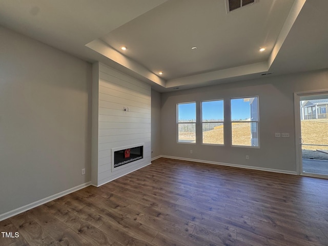 unfurnished living room featuring dark hardwood / wood-style floors, a large fireplace, and a tray ceiling