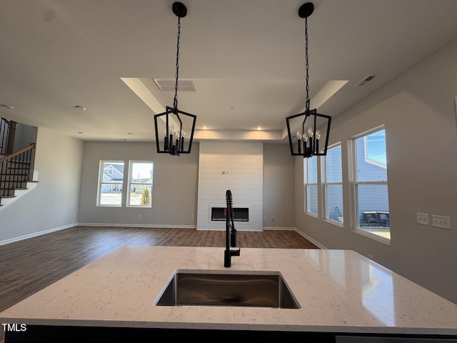 kitchen featuring pendant lighting, light stone countertops, and a center island with sink