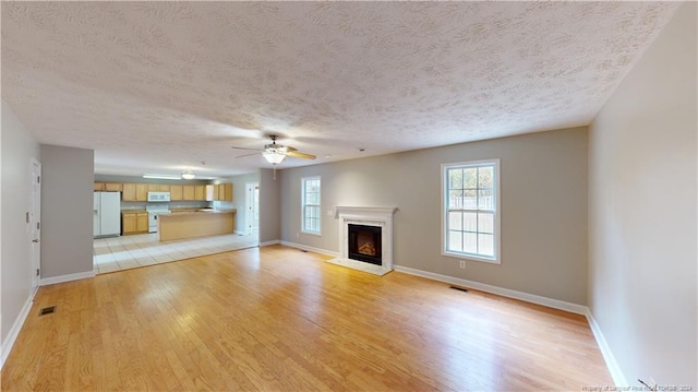 unfurnished living room with ceiling fan, light hardwood / wood-style floors, and a textured ceiling