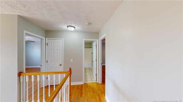 hall with light wood-type flooring and a textured ceiling