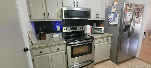 kitchen with white cabinetry, light stone counters, decorative backsplash, light tile patterned flooring, and appliances with stainless steel finishes