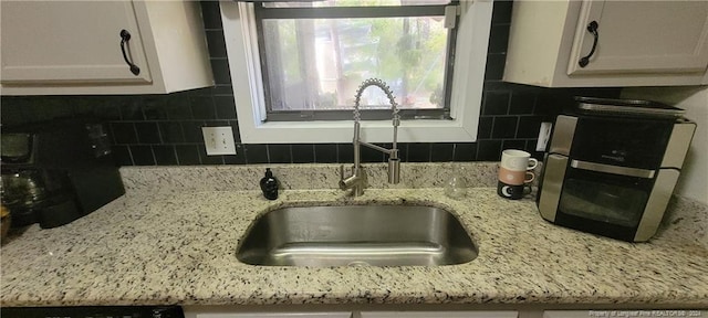 kitchen featuring decorative backsplash, light stone countertops, white cabinetry, and sink