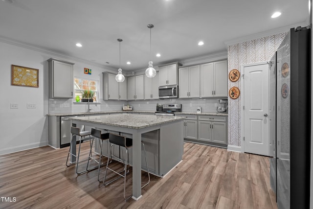 kitchen with pendant lighting, stainless steel appliances, a kitchen island, and ornamental molding