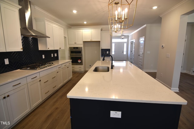 kitchen with dark wood-style flooring, stainless steel appliances, ornamental molding, a sink, and wall chimney exhaust hood