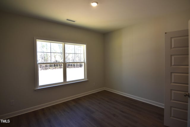 spare room with dark wood-style flooring, visible vents, and baseboards