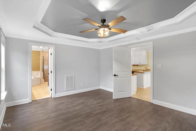 unfurnished bedroom featuring hardwood / wood-style flooring, ensuite bath, ceiling fan, and a tray ceiling