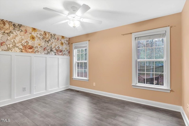 empty room with dark wood-type flooring, ceiling fan, and a healthy amount of sunlight