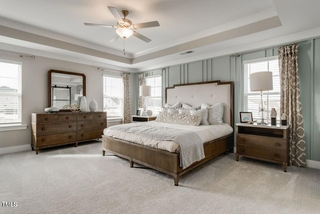 carpeted bedroom featuring a raised ceiling, ceiling fan, and multiple windows